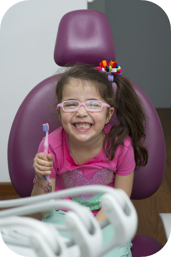Smiling child in dentist's chair, holding a toothbrush in her right hand